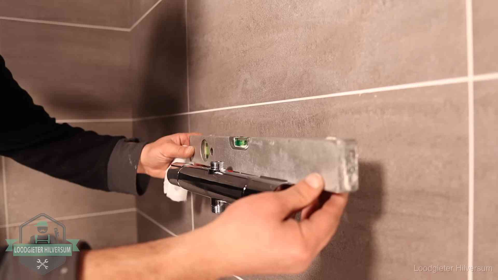 Loodgieter lijnt een douchekraan uit met een waterpas in een woning in Hilversum