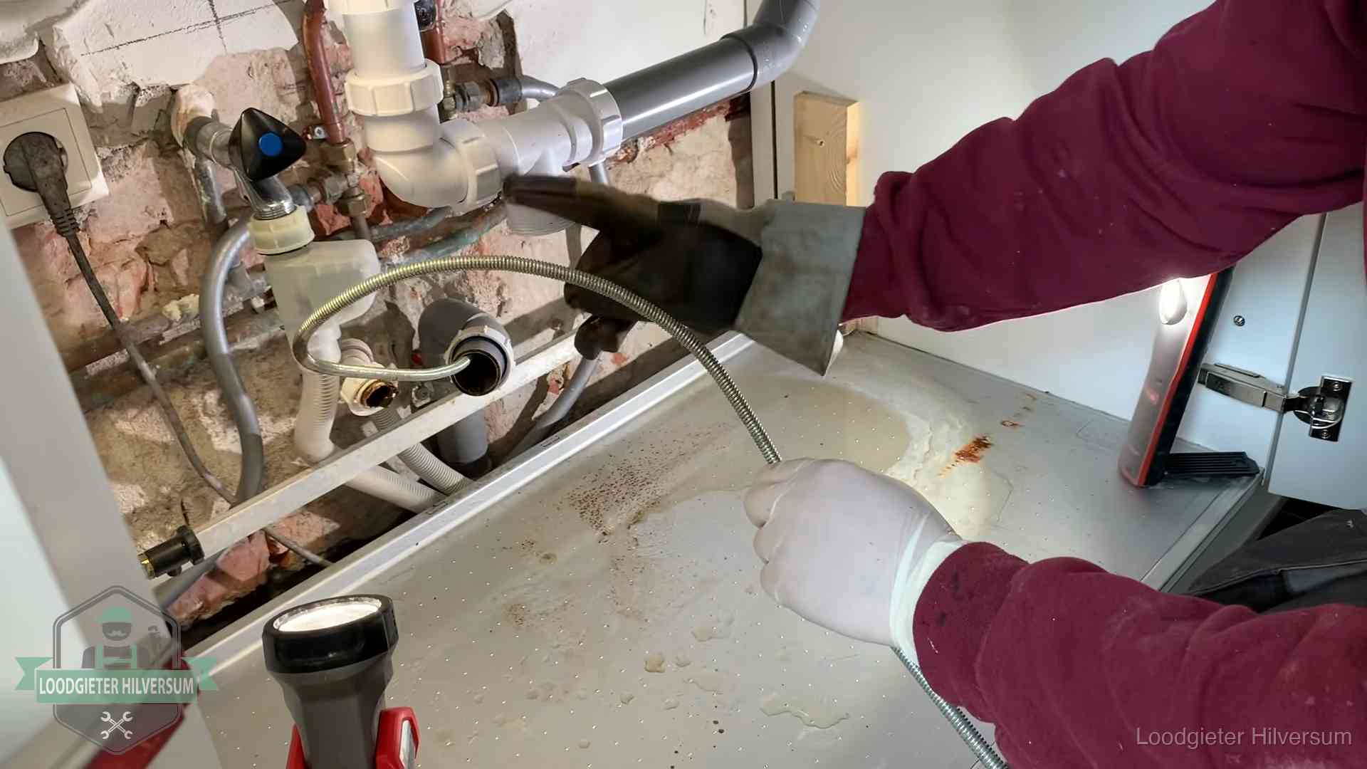 Ontstoppingsveer gaat in een geopende sifonaansluiting onder het aanrecht in Hilversum
