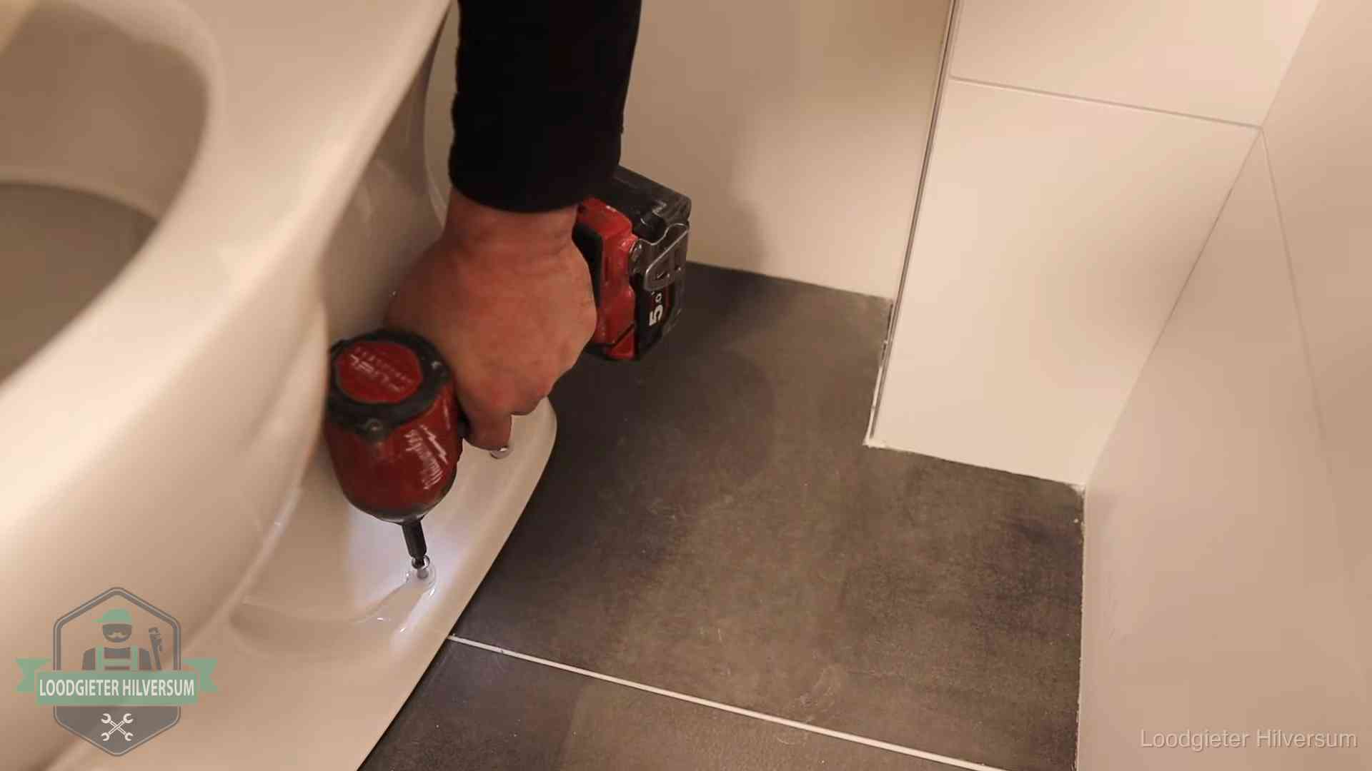 Kosten wc ontstoppen in Hilversum Loodgieter zet de voet van een wc-pot vast op de tegelvloer in Hilversum